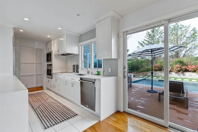 kitchen with white cabinets, sink, decorative backsplash, light wood-type flooring, and stainless steel appliances