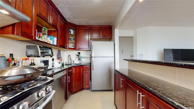 kitchen featuring appliances with stainless steel finishes, sink, light tile patterned floors, and dark stone countertops