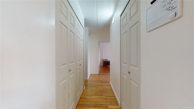 hallway with light wood-type flooring and a textured ceiling