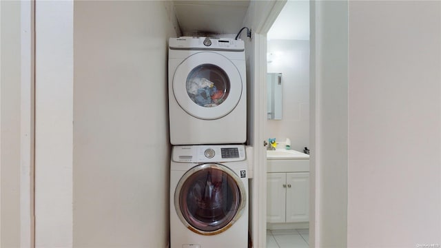 laundry room featuring sink, light tile patterned floors, and stacked washing maching and dryer