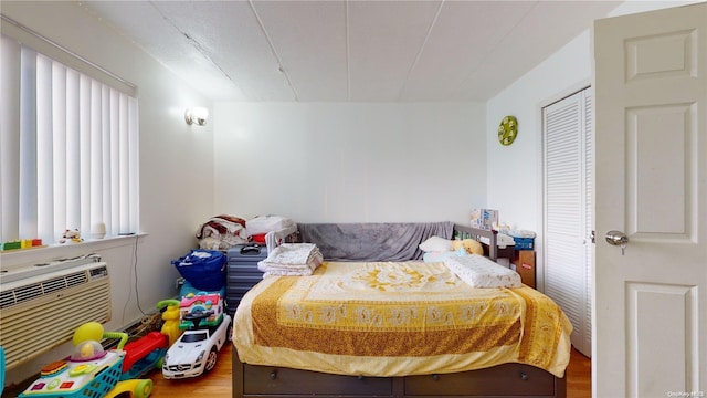 bedroom featuring hardwood / wood-style floors, an AC wall unit, and multiple windows