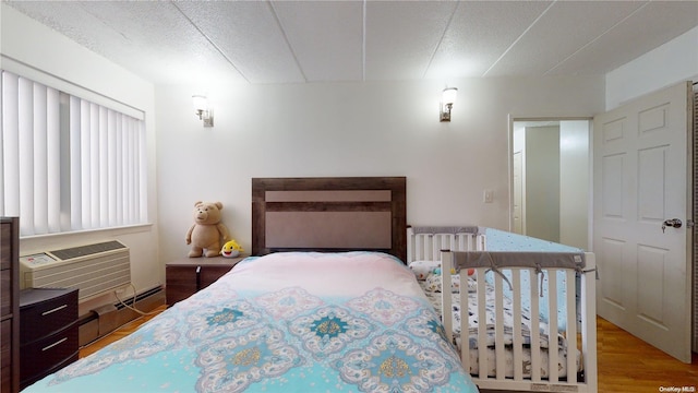 bedroom featuring hardwood / wood-style floors, a wall mounted air conditioner, a textured ceiling, and a baseboard heating unit