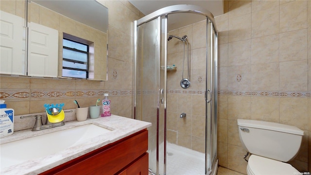 bathroom featuring vanity, toilet, a shower with shower door, and tile walls