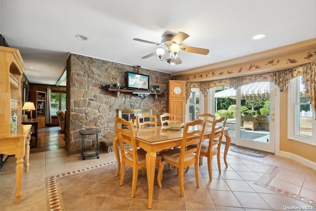 dining area featuring tile patterned floors, a stone fireplace, and ceiling fan