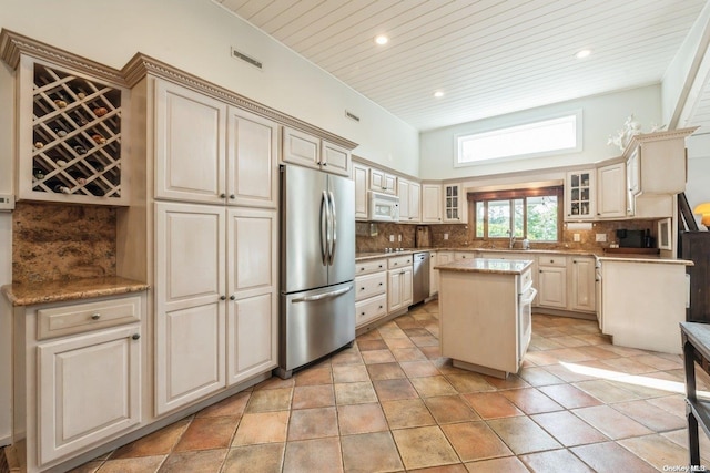 kitchen with decorative backsplash, appliances with stainless steel finishes, cream cabinetry, and a kitchen island