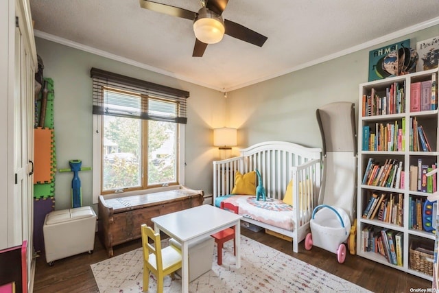 bedroom featuring ceiling fan, dark hardwood / wood-style flooring, a textured ceiling, a nursery area, and ornamental molding