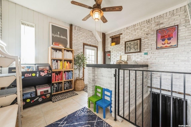 recreation room with tile patterned flooring, ceiling fan, and brick wall