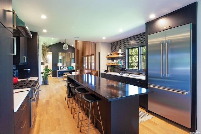 kitchen featuring premium appliances, a kitchen island, light hardwood / wood-style floors, and vaulted ceiling