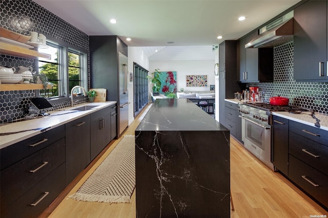 kitchen with tasteful backsplash, a spacious island, sink, light hardwood / wood-style flooring, and high end stainless steel range