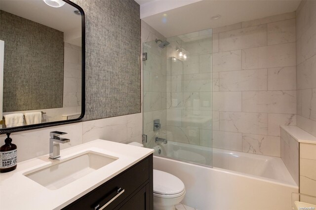 full bathroom with vanity, toilet, tile walls, and bath / shower combo with glass door