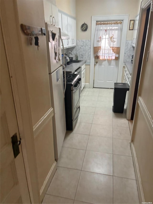 kitchen featuring white cabinets, sink, gas range, light tile patterned floors, and white fridge