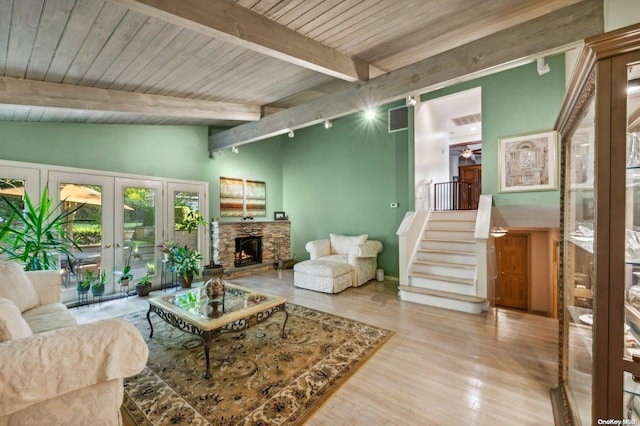 living room featuring vaulted ceiling with beams, a stone fireplace, french doors, and light wood-type flooring