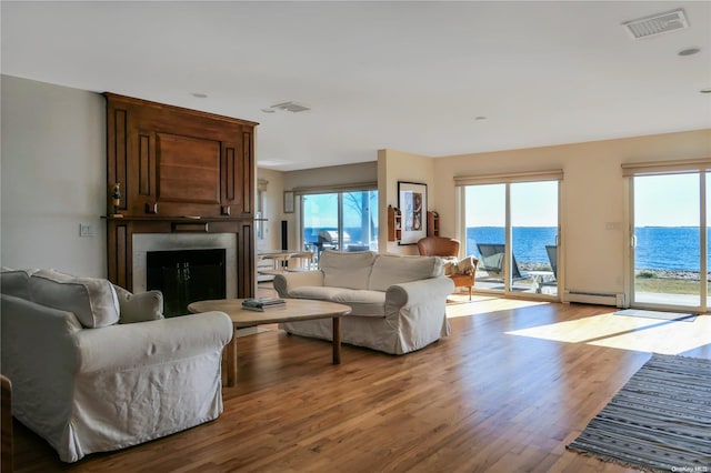 living room with a fireplace, a baseboard heating unit, a water view, and light hardwood / wood-style floors