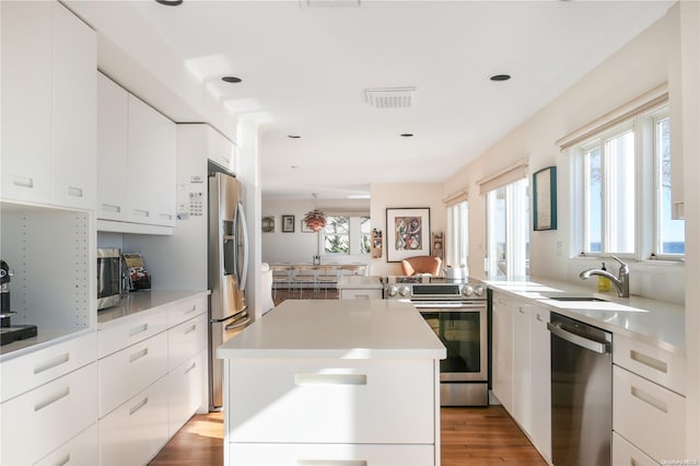 kitchen with white cabinetry, sink, light hardwood / wood-style floors, a kitchen island, and appliances with stainless steel finishes