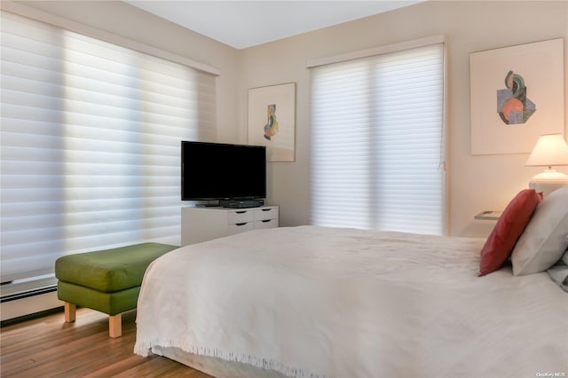 bedroom featuring multiple windows, light hardwood / wood-style floors, and baseboard heating