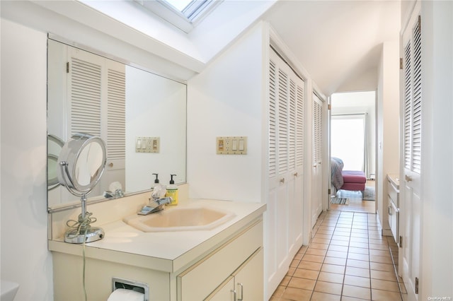 bathroom featuring tile patterned flooring, vanity, and vaulted ceiling with skylight