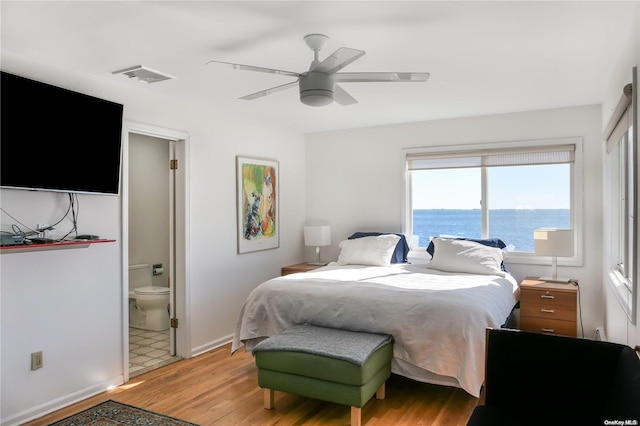 bedroom with ensuite bath, ceiling fan, light hardwood / wood-style flooring, and a water view