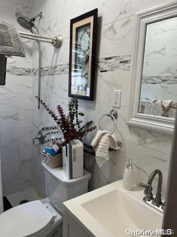 bathroom featuring a tile shower, toilet, decorative backsplash, vanity, and tile walls