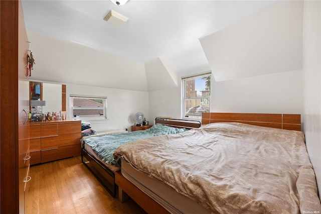 bedroom with multiple windows, lofted ceiling, and light wood-type flooring