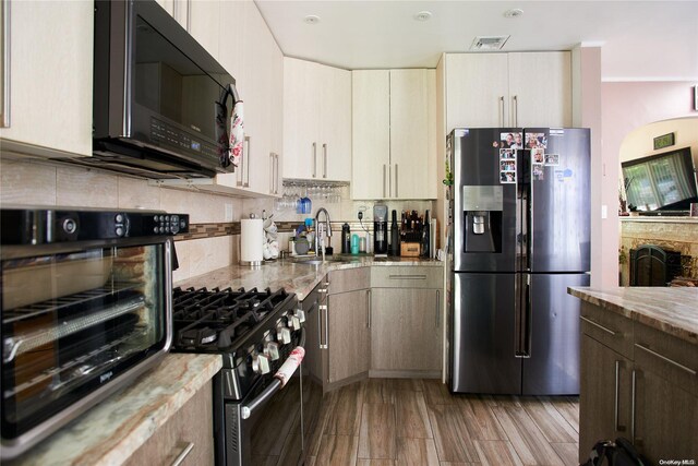 kitchen featuring backsplash, light stone counters, stainless steel appliances, sink, and light hardwood / wood-style floors