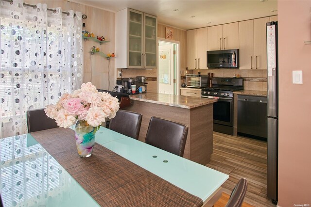 kitchen featuring light stone countertops, kitchen peninsula, decorative backsplash, appliances with stainless steel finishes, and light wood-type flooring