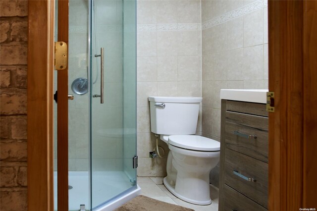 bathroom with vanity, a shower with door, tile patterned floors, toilet, and tile walls