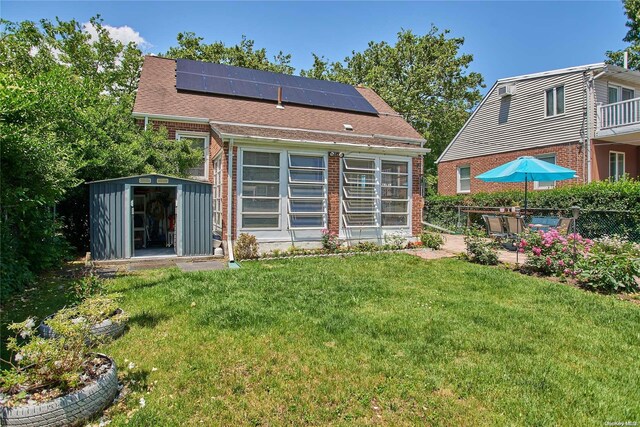 back of house with solar panels, a shed, and a lawn