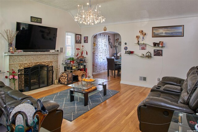 living room featuring an inviting chandelier, a textured ceiling, lofted ceiling, a fireplace, and hardwood / wood-style flooring