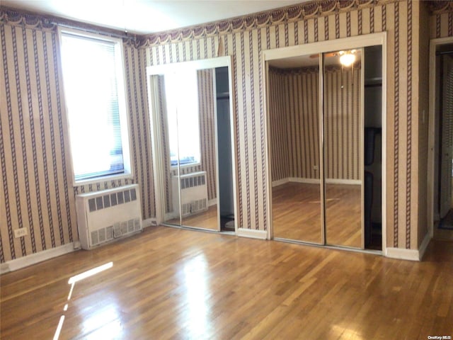 unfurnished bedroom with multiple windows, radiator heating unit, and hardwood / wood-style floors