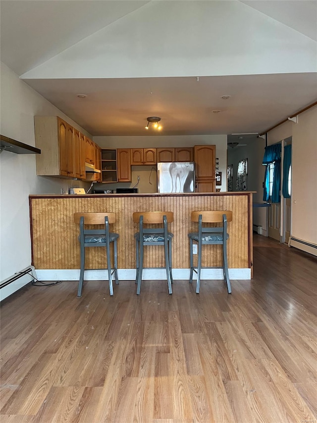 kitchen featuring kitchen peninsula, light hardwood / wood-style floors, stainless steel refrigerator, and a breakfast bar area