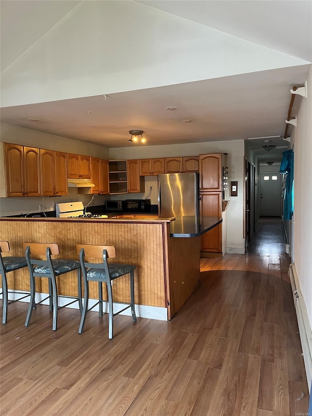 kitchen featuring kitchen peninsula, stainless steel fridge, a breakfast bar, and dark hardwood / wood-style flooring