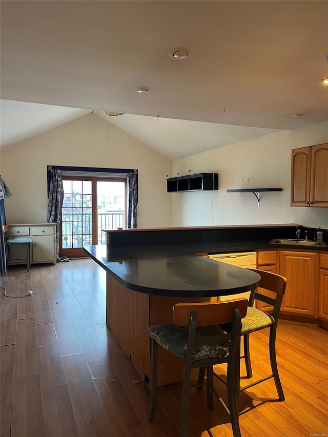 kitchen featuring lofted ceiling, a kitchen bar, light wood-type flooring, and sink