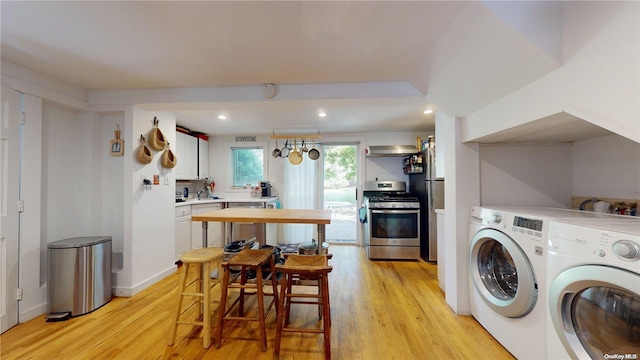 clothes washing area with washing machine and dryer and light wood-type flooring