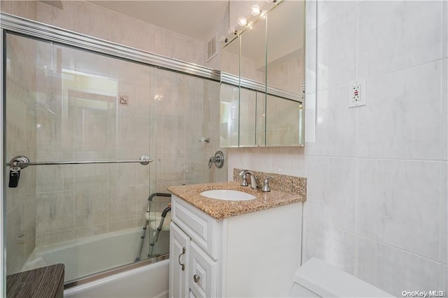 bathroom featuring vanity, tile walls, and bath / shower combo with glass door