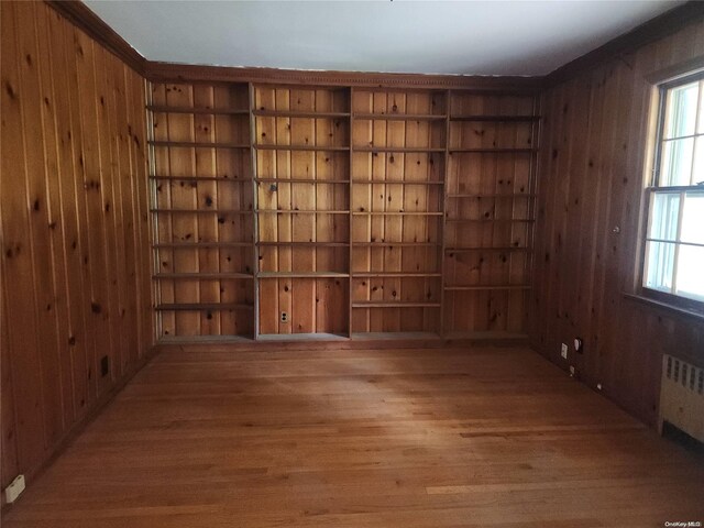 unfurnished room with wood-type flooring, radiator, crown molding, and wood walls