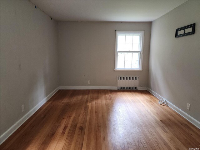 unfurnished room featuring hardwood / wood-style floors and radiator heating unit