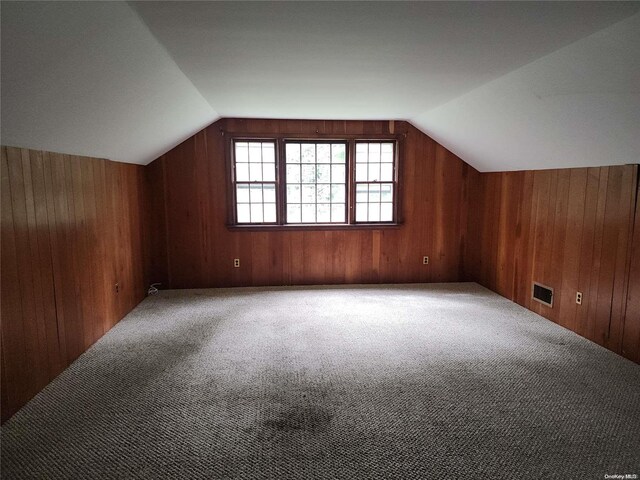 additional living space with wood walls, carpet, and vaulted ceiling