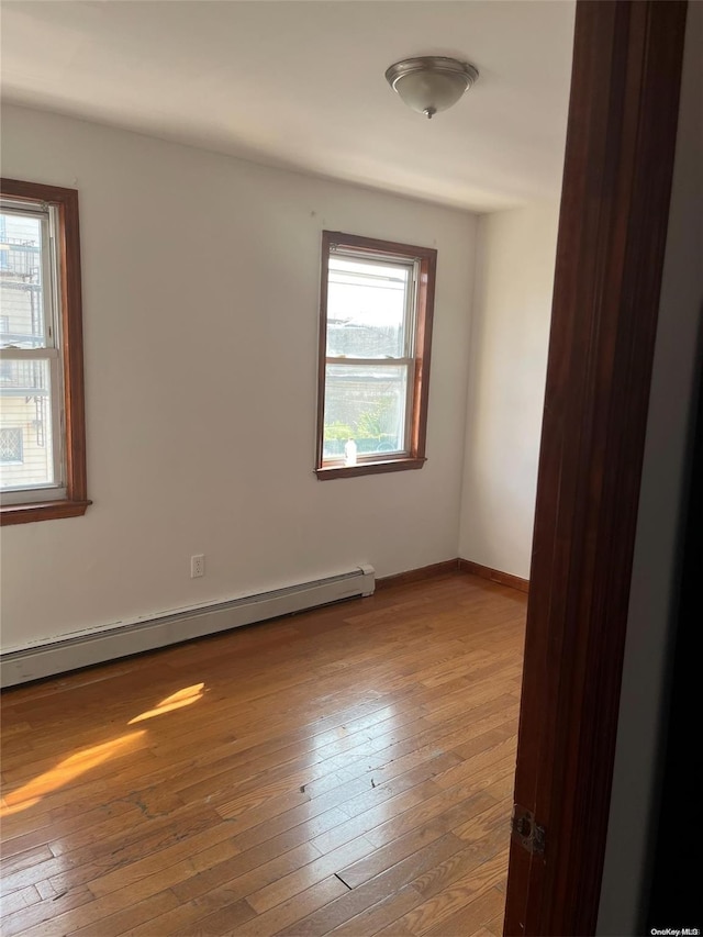 empty room with plenty of natural light, hardwood / wood-style floors, and a baseboard radiator