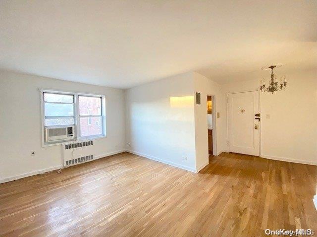 empty room featuring radiator heating unit, light hardwood / wood-style floors, an inviting chandelier, and cooling unit