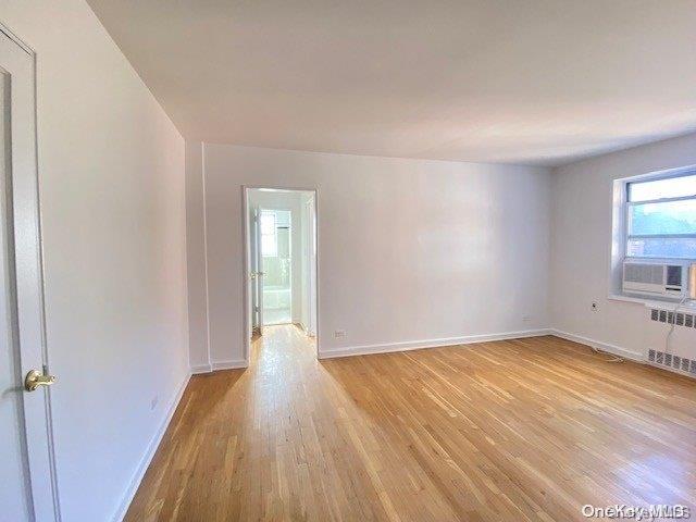 spare room with radiator, cooling unit, and light wood-type flooring