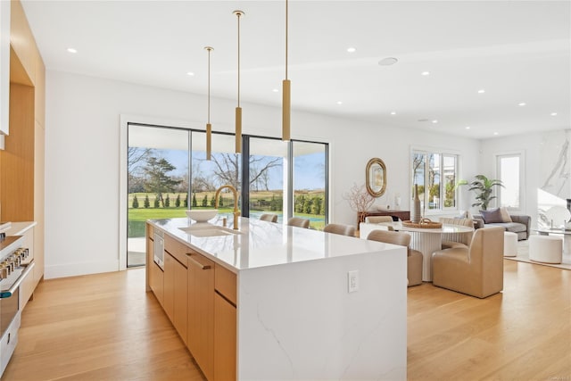 kitchen with light stone countertops, a large island, sink, hanging light fixtures, and light hardwood / wood-style flooring