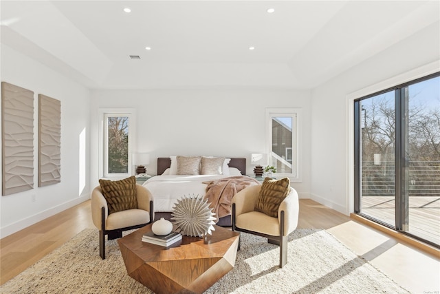 bedroom featuring a tray ceiling, access to exterior, and light hardwood / wood-style floors