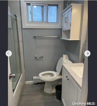 full bathroom with a baseboard heating unit, bath / shower combo with glass door, wood-type flooring, toilet, and vanity