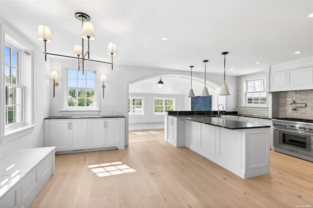 kitchen featuring pendant lighting, high end range, a kitchen island with sink, white cabinets, and light hardwood / wood-style floors