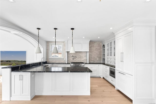 kitchen featuring kitchen peninsula, hanging light fixtures, appliances with stainless steel finishes, and light hardwood / wood-style flooring