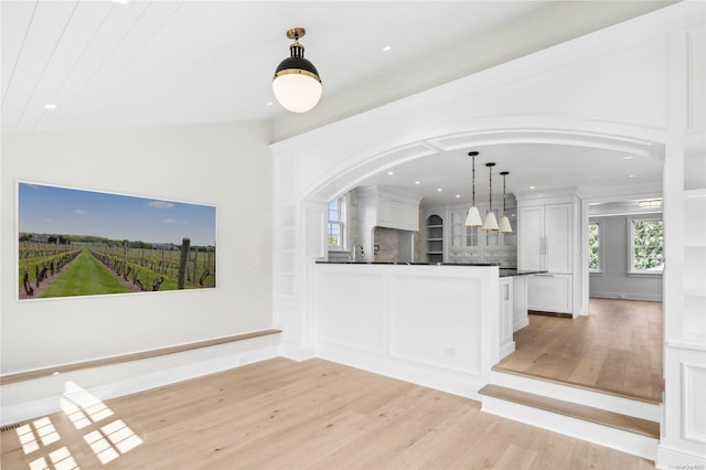 interior space featuring pendant lighting, white cabinets, vaulted ceiling, decorative backsplash, and light hardwood / wood-style floors