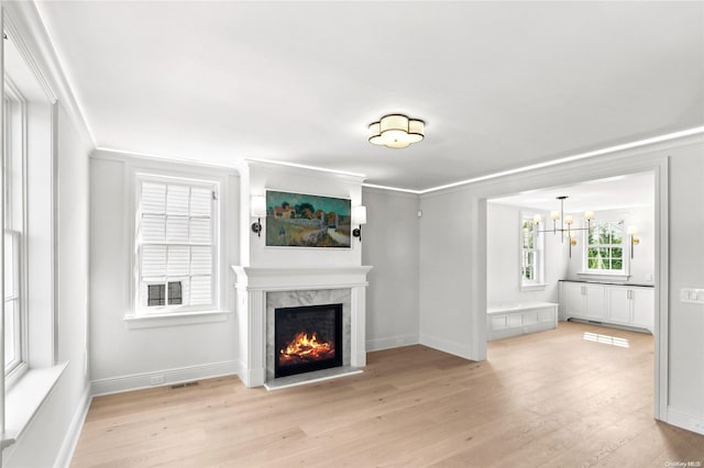 unfurnished living room with light hardwood / wood-style floors, a premium fireplace, crown molding, and a chandelier