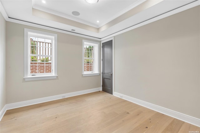 empty room with a tray ceiling, light hardwood / wood-style floors, and ornamental molding