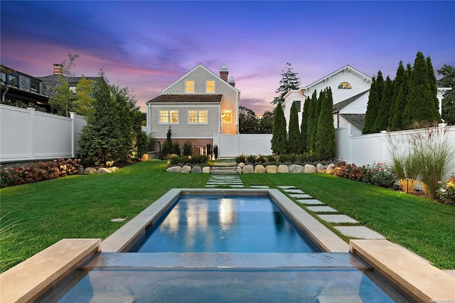 back house at dusk with a fenced in pool and a lawn