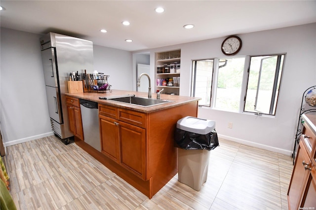 kitchen with a center island with sink, built in shelves, sink, and stainless steel appliances